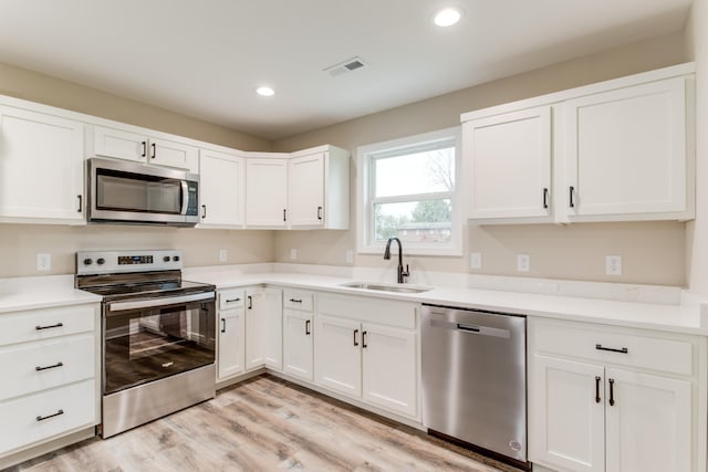 kitchen featuring appliances with stainless steel finishes, light wood-type flooring, white cabinetry, and sink