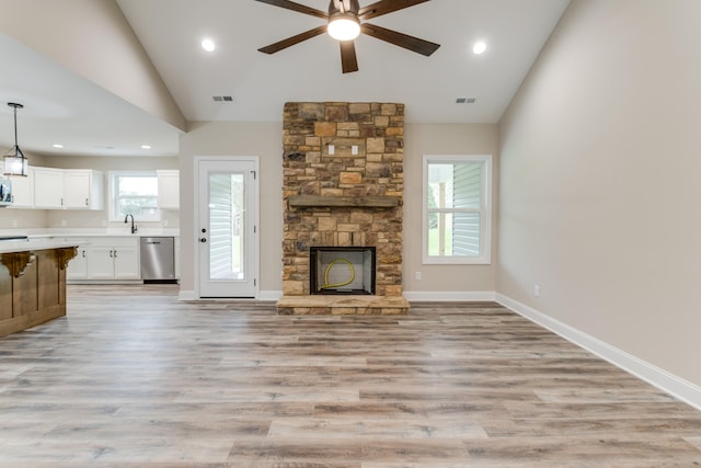 unfurnished living room with light wood-type flooring, a stone fireplace, ceiling fan, and lofted ceiling