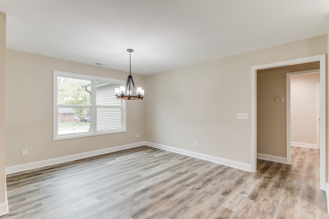 empty room with light wood-type flooring and a notable chandelier