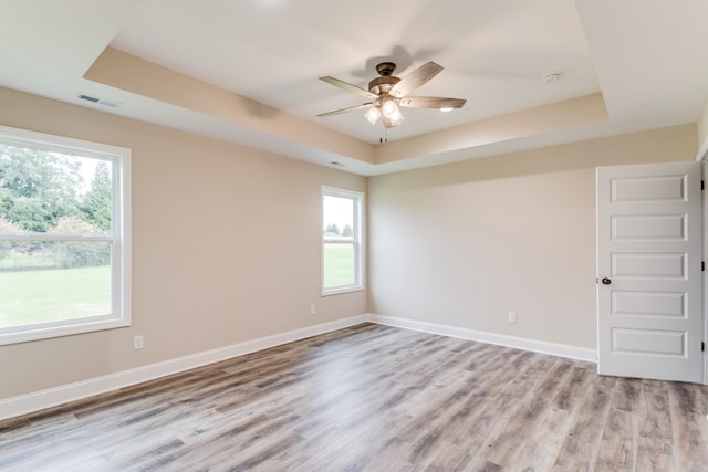 unfurnished room featuring a raised ceiling, ceiling fan, and light hardwood / wood-style floors