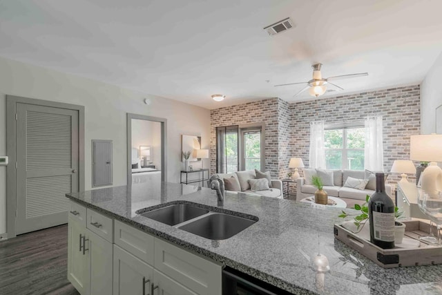 kitchen with light stone counters, sink, dark hardwood / wood-style flooring, ceiling fan, and brick wall