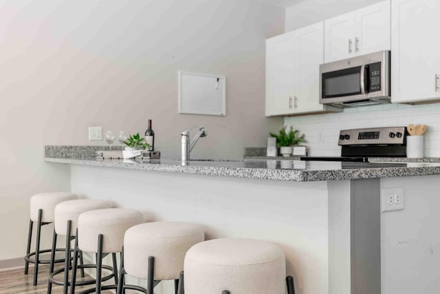 kitchen with appliances with stainless steel finishes, white cabinetry, hardwood / wood-style floors, and a breakfast bar