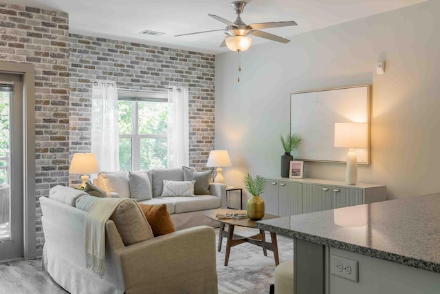 living room featuring ceiling fan, light hardwood / wood-style flooring, and brick wall