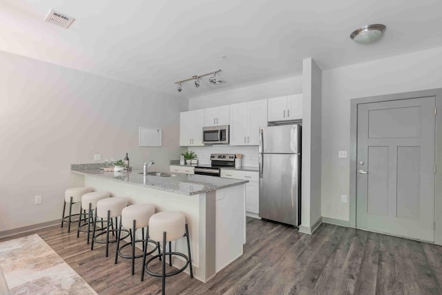 kitchen with a breakfast bar, sink, white cabinetry, appliances with stainless steel finishes, and dark hardwood / wood-style flooring