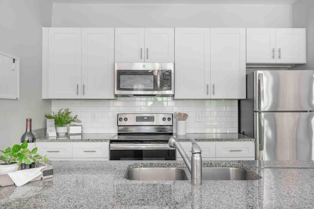 kitchen with light stone counters, stainless steel appliances, sink, and white cabinetry