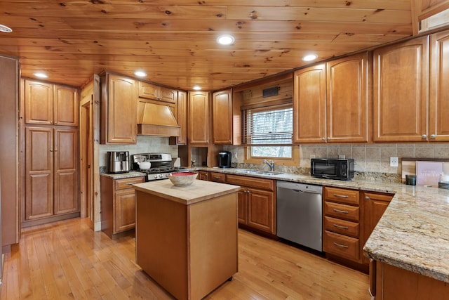 kitchen featuring light stone counters, a kitchen island, light hardwood / wood-style flooring, stainless steel appliances, and premium range hood