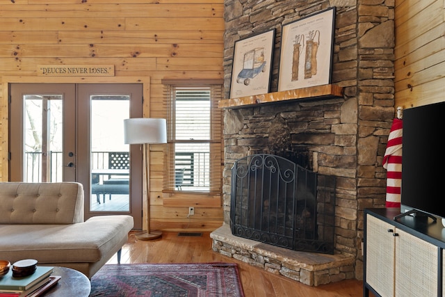 living room with a stone fireplace, hardwood / wood-style flooring, and wooden walls