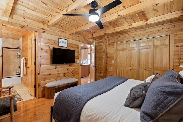 bedroom with a closet, light hardwood / wood-style floors, beam ceiling, wooden walls, and ceiling fan