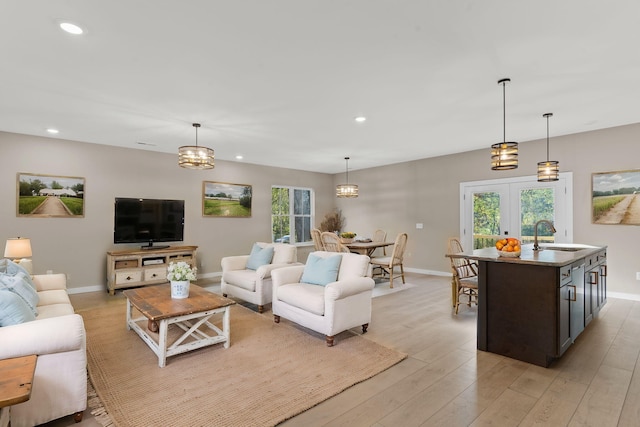 living room with light hardwood / wood-style floors, a wealth of natural light, a notable chandelier, and sink