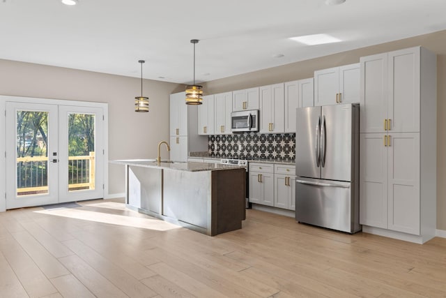 kitchen with appliances with stainless steel finishes, light stone counters, light hardwood / wood-style flooring, white cabinets, and an island with sink