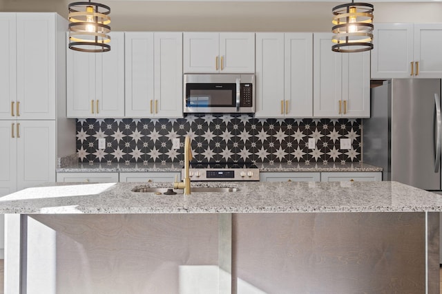 kitchen with appliances with stainless steel finishes, light stone counters, sink, white cabinets, and hanging light fixtures