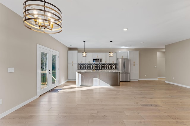 kitchen featuring appliances with stainless steel finishes, backsplash, french doors, a center island with sink, and white cabinetry