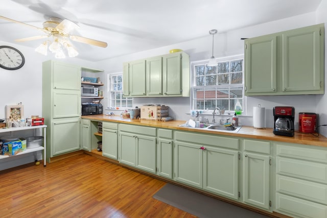 kitchen featuring ceiling fan, sink, green cabinetry, decorative light fixtures, and light wood-type flooring