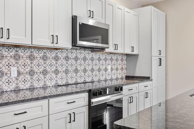 kitchen with white cabinets, stove, backsplash, and dark stone countertops