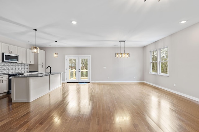 kitchen featuring white cabinetry, french doors, backsplash, an island with sink, and decorative light fixtures