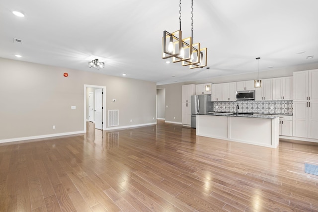 unfurnished living room with sink, a notable chandelier, and light wood-type flooring