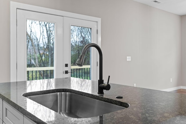 room details with white cabinets, dark stone counters, and sink