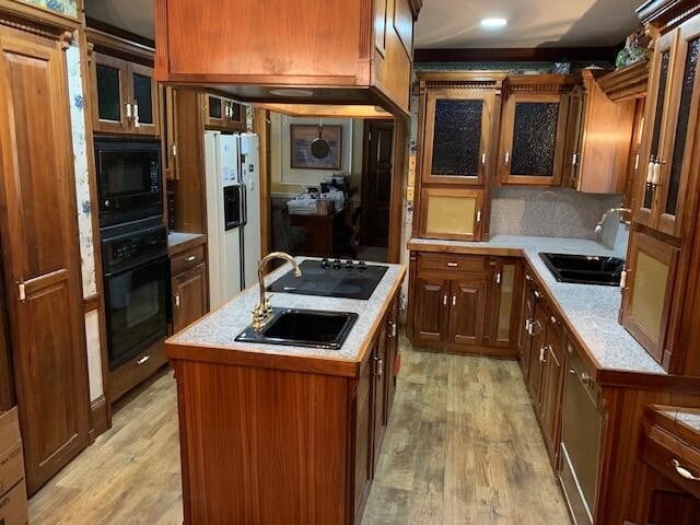 kitchen with light hardwood / wood-style floors, sink, backsplash, black appliances, and a center island with sink