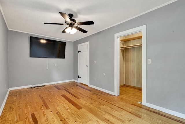 unfurnished bedroom with a textured ceiling, hardwood / wood-style floors, ceiling fan, and a walk in closet