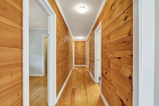 hall featuring a textured ceiling, ornamental molding, wooden walls, and light hardwood / wood-style flooring