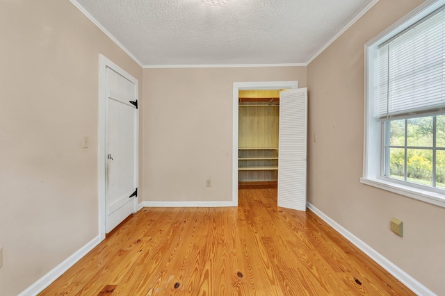 unfurnished bedroom with light wood-type flooring, a closet, a textured ceiling, a walk in closet, and crown molding