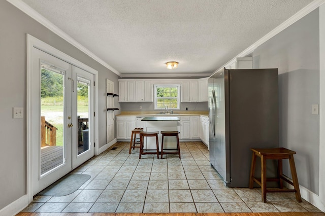 kitchen featuring stainless steel refrigerator with ice dispenser, a kitchen bar, white cabinetry, and plenty of natural light