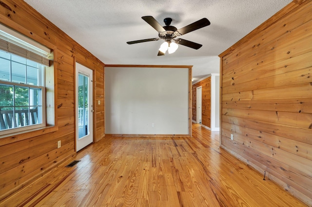 unfurnished room with ceiling fan, a textured ceiling, wood walls, and light hardwood / wood-style floors