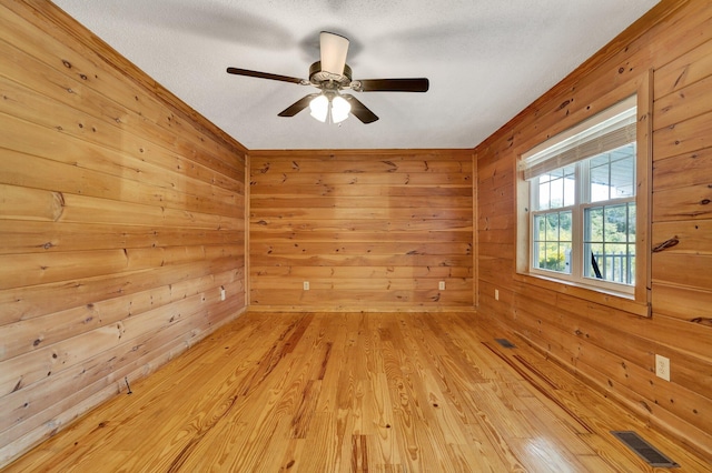 spare room with light hardwood / wood-style flooring, wood walls, ceiling fan, and a textured ceiling