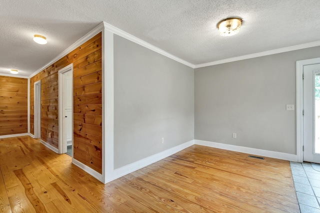 spare room featuring light wood-type flooring, ornamental molding, a textured ceiling, and wooden walls