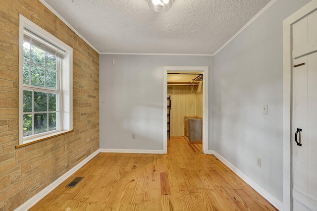 unfurnished bedroom featuring a textured ceiling, light hardwood / wood-style floors, ornamental molding, and a spacious closet