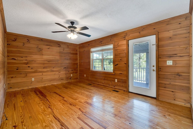 spare room featuring ceiling fan, a textured ceiling, wooden walls, and light hardwood / wood-style floors