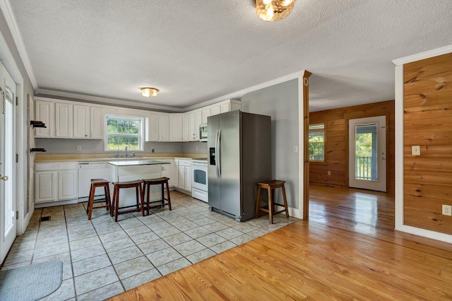 kitchen with stainless steel appliances, wood walls, light hardwood / wood-style floors, and white cabinets