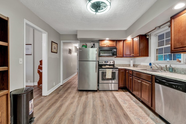 kitchen with a textured ceiling, appliances with stainless steel finishes, light wood-type flooring, and sink