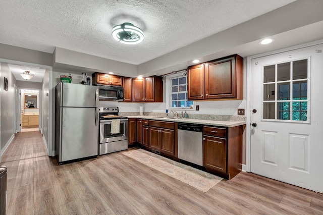 kitchen with a textured ceiling, sink, light hardwood / wood-style flooring, and stainless steel appliances