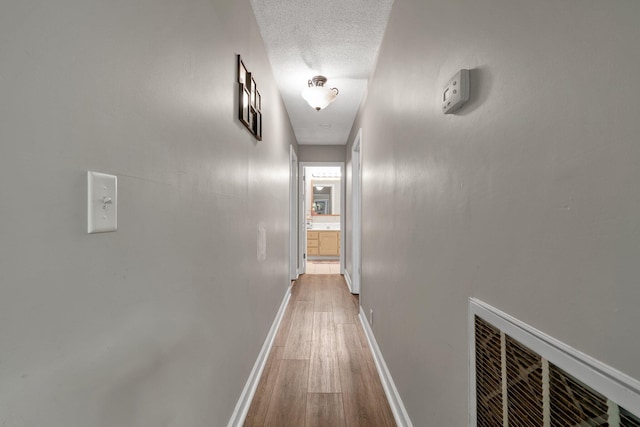 hall with a textured ceiling and light hardwood / wood-style flooring