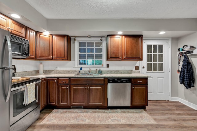 kitchen featuring a textured ceiling, stainless steel appliances, light wood-type flooring, and sink