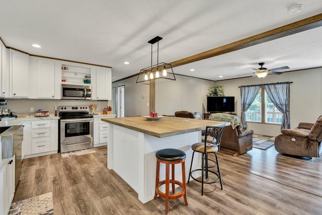 kitchen with pendant lighting, stainless steel appliances, white cabinetry, and light hardwood / wood-style flooring