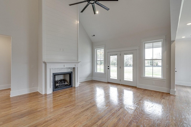 unfurnished living room featuring high vaulted ceiling, light wood-type flooring, a high end fireplace, and ceiling fan