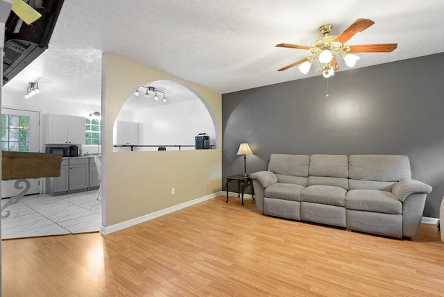 living room with a textured ceiling, light hardwood / wood-style floors, and ceiling fan