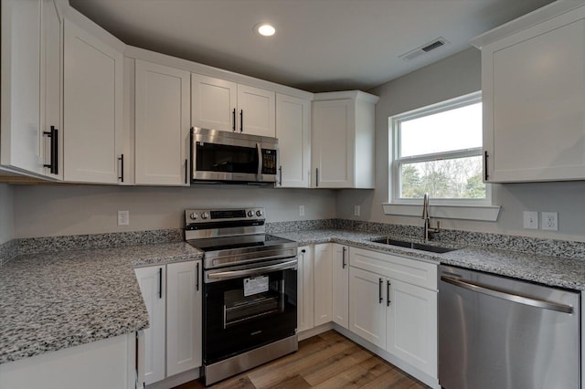 kitchen featuring sink, white cabinetry, light stone counters, appliances with stainless steel finishes, and light hardwood / wood-style floors