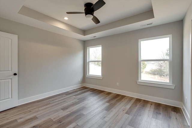 empty room with ceiling fan, a raised ceiling, and light hardwood / wood-style flooring