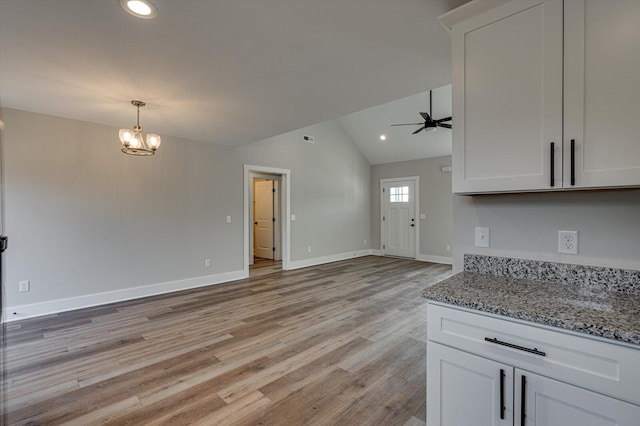 kitchen featuring white cabinetry, vaulted ceiling, light stone countertops, and ceiling fan with notable chandelier