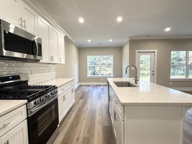 kitchen with light wood-type flooring, stainless steel appliances, a wealth of natural light, and an island with sink