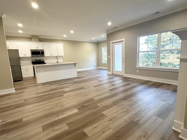 kitchen with appliances with stainless steel finishes, white cabinetry, a kitchen island with sink, light hardwood / wood-style flooring, and sink