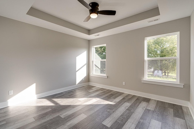 empty room with a raised ceiling, hardwood / wood-style floors, and ceiling fan