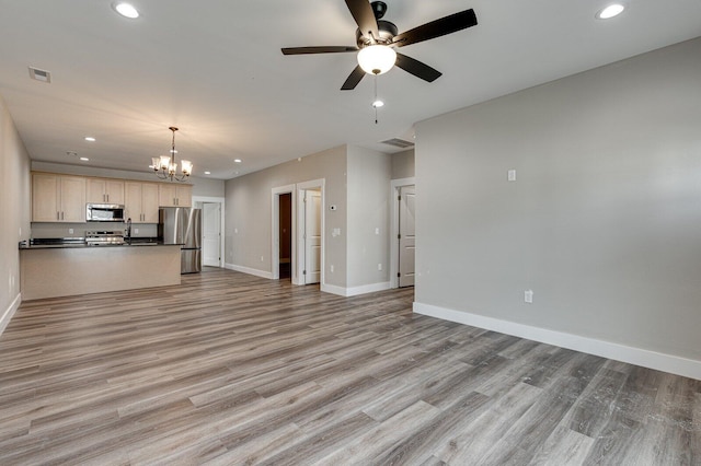 unfurnished living room with ceiling fan with notable chandelier and light wood-type flooring