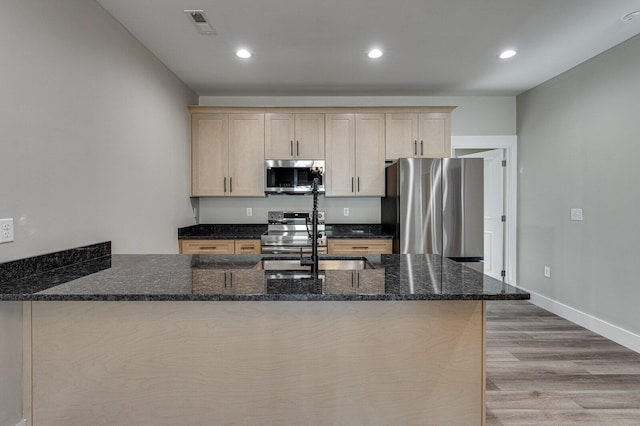 kitchen with stainless steel appliances, light hardwood / wood-style flooring, light brown cabinets, and dark stone counters