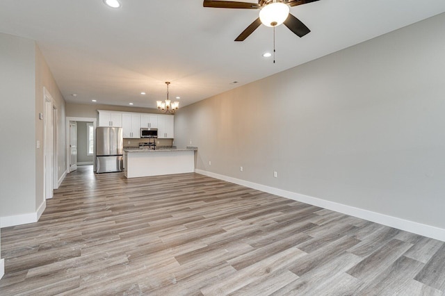 unfurnished living room featuring ceiling fan with notable chandelier and light wood-type flooring