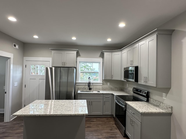 kitchen with light stone counters, a kitchen island, appliances with stainless steel finishes, gray cabinets, and sink