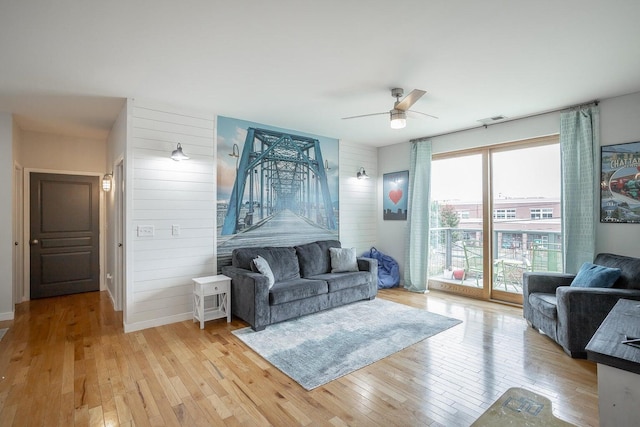 living room with wooden walls, ceiling fan, and light hardwood / wood-style floors